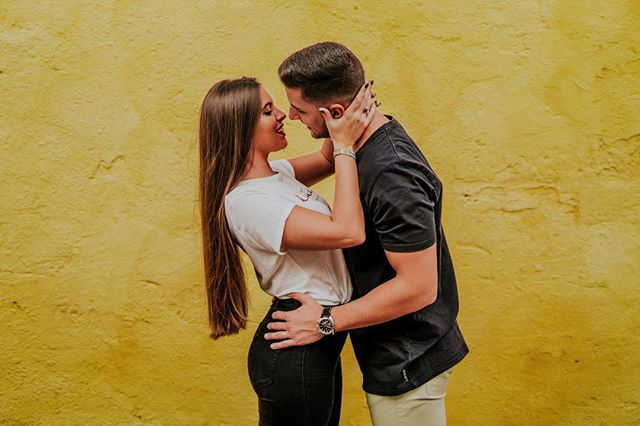 A young couple in love embraces against a vibrant yellow wall, sharing a tender and intimate moment.