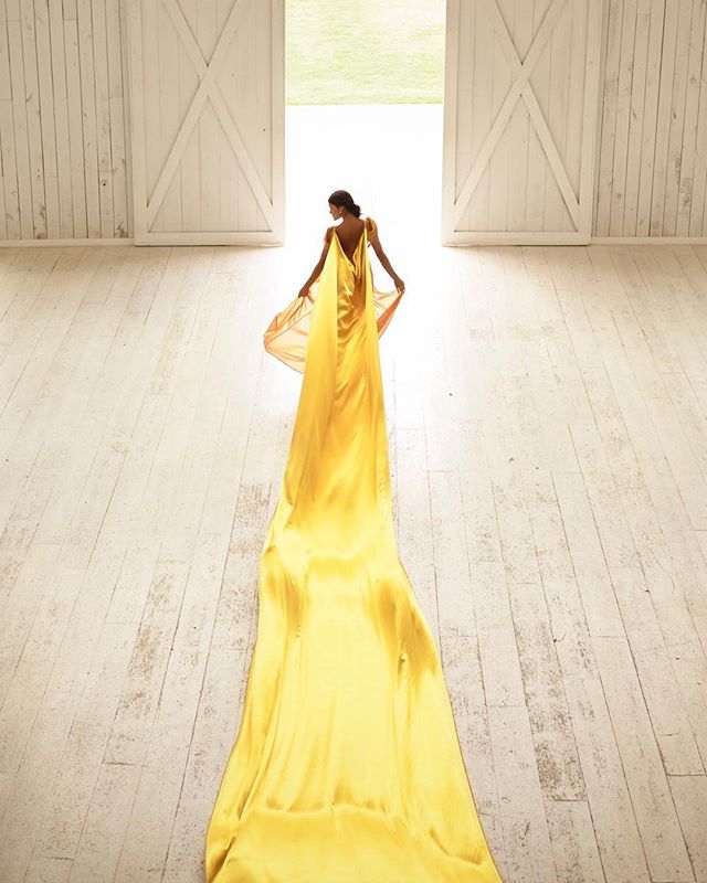 A woman in a yellow dress stands in a doorway of an airy barn.