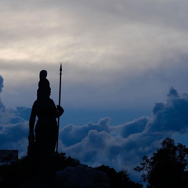 Silhouette of a statue with a spear against a cloudy sky on a mountain. A serene travel and cultural tourism destination.