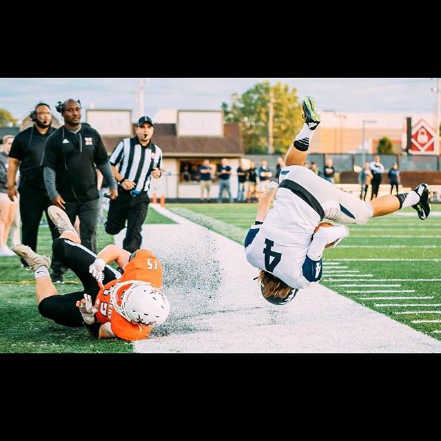A football player flips over another player during a game on a sunny day.