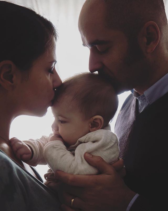 A loving mother and father gently kiss their baby's forehead in a tender family moment.