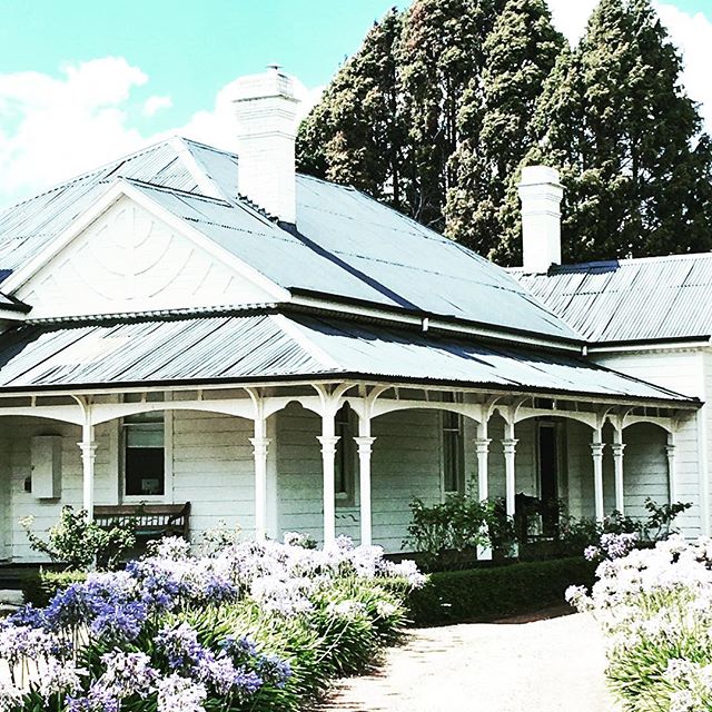 A charming white house with a porch and a beautiful garden filled with blue and white flowers, creating a serene setting.