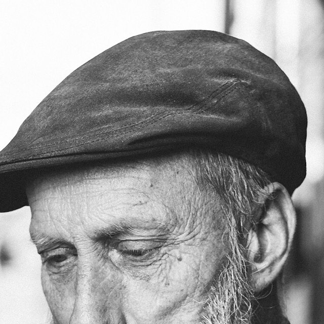 Close-up black and white portrait of an elderly man wearing a cap, conveying a thoughtful and emotional mood.