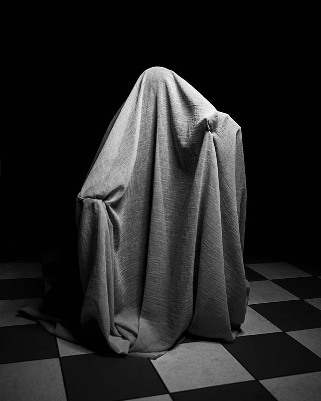 Monochromatic image of a figure draped in fabric, evoking mystery and artistry in a minimalist setting.