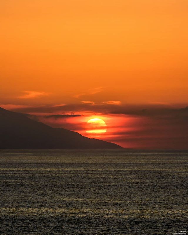A scenic view of a sunset over the ocean, with a silhouette of a mountain in the background.