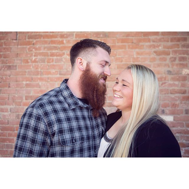A happy couple shares a loving moment against a brick wall, full of warmth and joy.