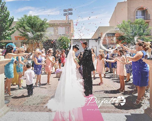 Bride and groom celebrate with guests as confetti is thrown at their wedding ceremony on a city street.