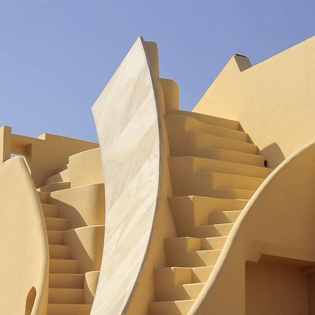Architectural detail showcasing stairs and geometric shapes in a warm, minimalist style under a clear blue sky.