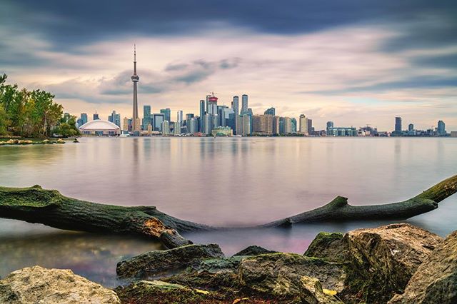 Toronto's iconic skyline featuring the CN Tower reflected in Lake Ontario under a cloudy sky. Tranquil city view.