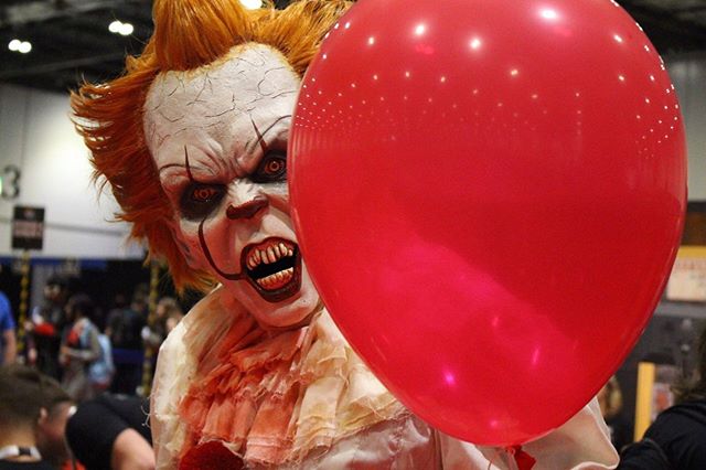 Cosplayer dressed as Pennywise holding a red balloon, creating a suspenseful, intense mood for Halloween or horror fans.