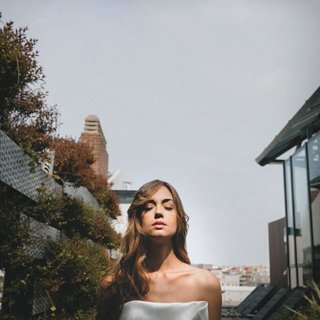 A serene woman with closed eyes stands on a rooftop, embracing a moment of tranquility amid the cityscape.