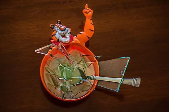 Tony the Tiger figurine stands over a bowl of frosted flakes cereal, which has been shattered with a spoon.