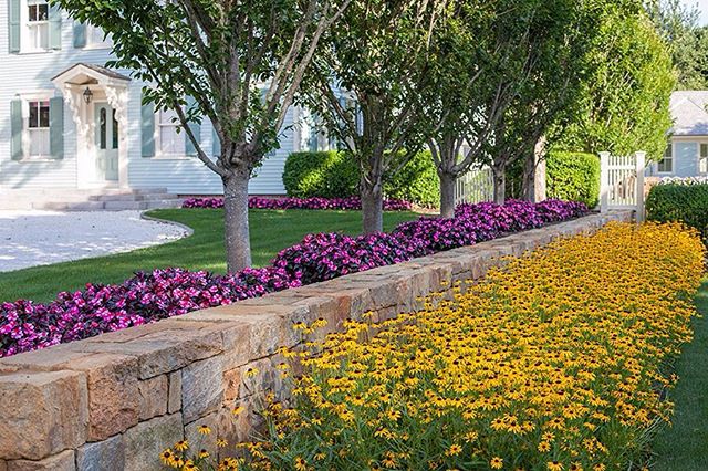 A colorful garden with a stone wall and vibrant flowers enhances the curb appeal of a charming home.
