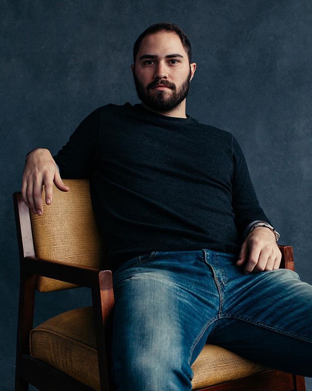 A man with a beard sits in a chair looking at the camera.