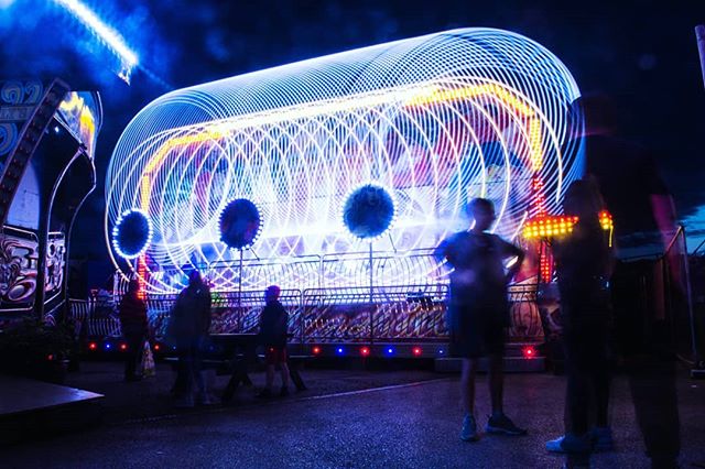 A vibrant long exposure image captures a spinning carnival ride at night, surrounded by people enjoying the fair.