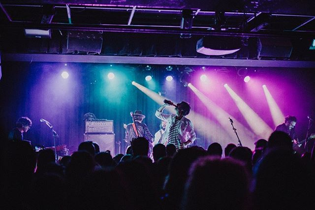 A band performs on stage under bright lights, entertaining a large crowd at a music venue.