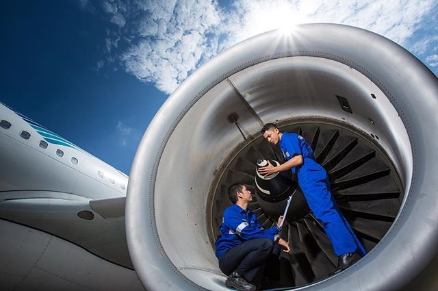 Two engineers inspect an aircraft engine against a blue sky, promoting aircraft maintenance and safety.