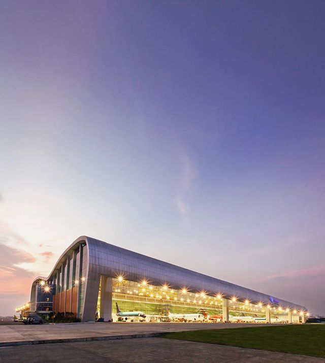 An airplane hangar filled with aircraft stands tall against a twilight sky, showcasing modern architecture.