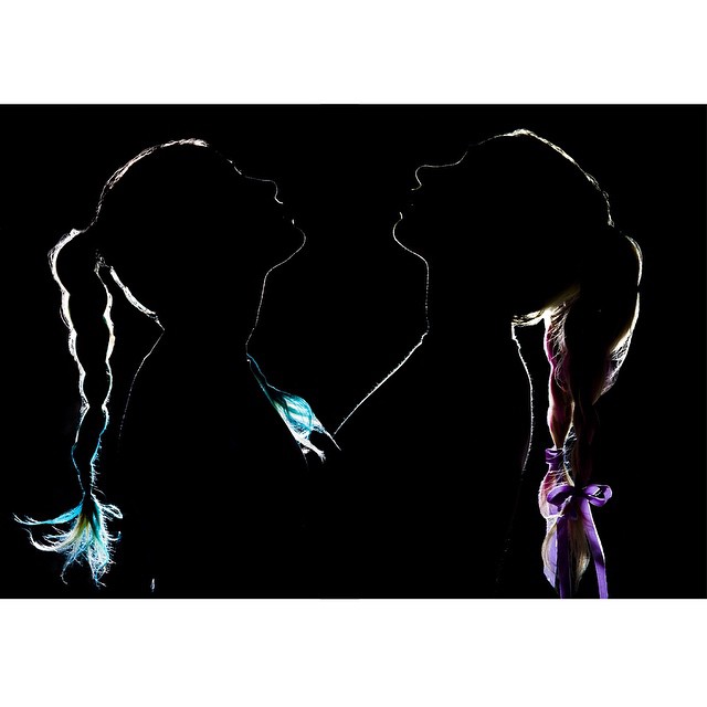 Silhouetted profiles of two girls with colorful braided hair against a dark background.