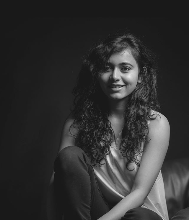 A young woman with curly hair poses in a black and white studio portrait.