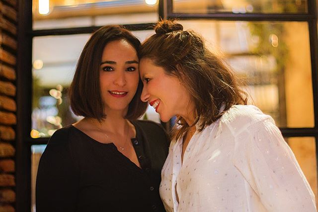 Two women share a loving moment, smiling warmly in an inviting indoor setting.