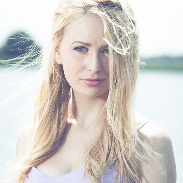 A blonde woman poses serenely near a lake, creating an image ideal for beauty or wellness campaigns.