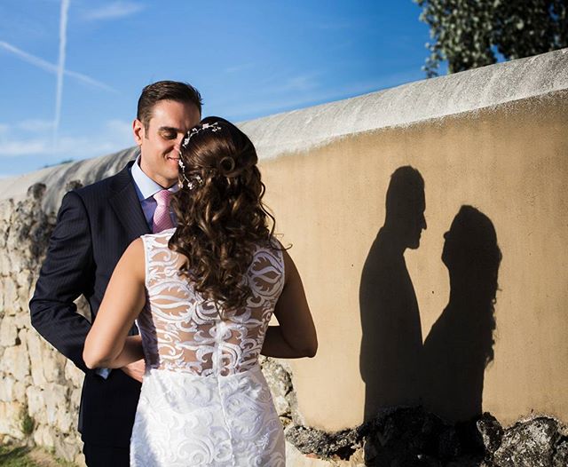 A bride and groom stand together, their shadows cast on a wall, creating a romantic and intimate moment.