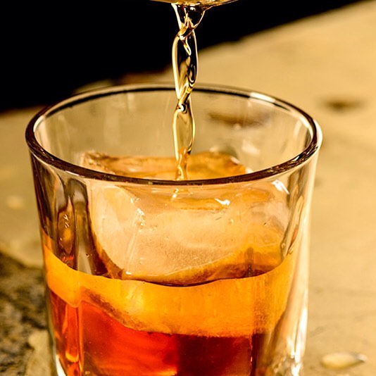 Whiskey is poured into a glass with ice in a warm, inviting atmosphere.