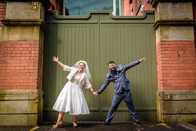 A cheerful bride and groom hold hands in front of a gate, celebrating their wedding with joy and love.