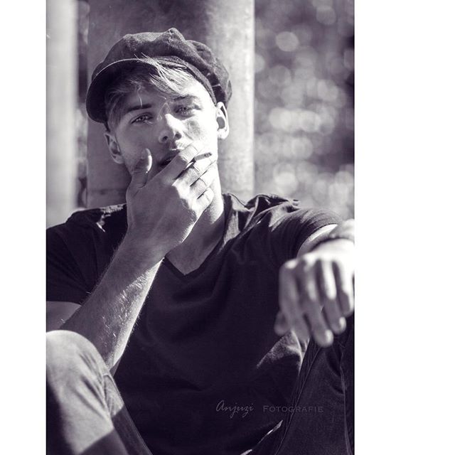 Black and white shot of a contemplative man wearing a cap, with a cigarette in hand.