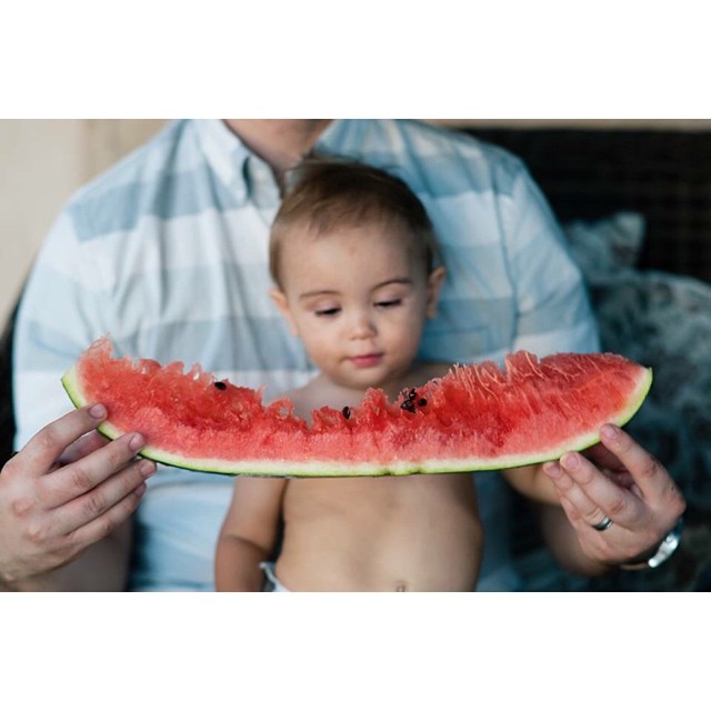 A baby and his father enjoy a slice of watermelon together, capturing a cheerful and playful moment.