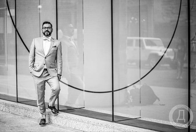 A man in a suit walks confidently in front of a modern building in black and white.