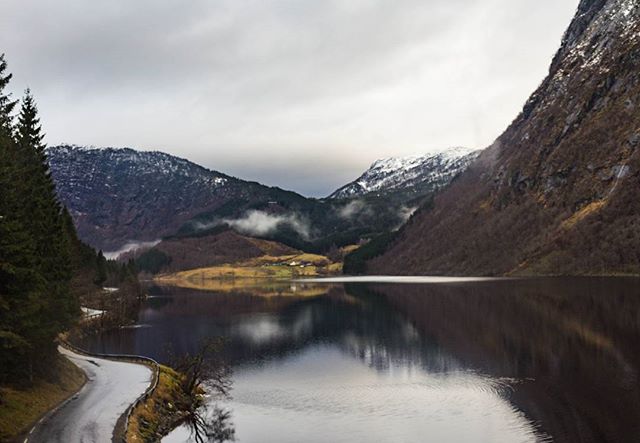 A winding road leads to a calm lake surrounded by mountains in a serene, natural landscape.