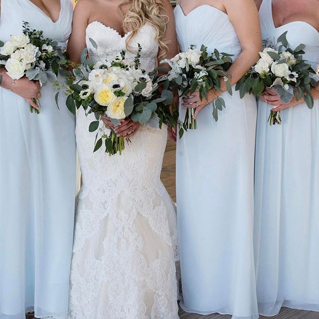 A bride and her bridesmaids in light blue dresses holding white and yellow flower bouquets at a wedding.