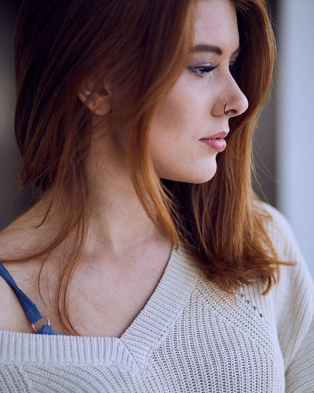 A redhead woman gazes thoughtfully in a softly lit portrait showcasing natural beauty and editorial style.
