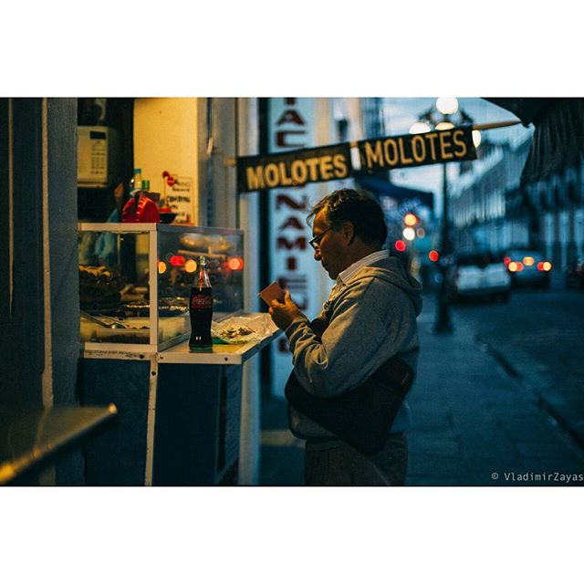 A man orders at a food stall at night, a Coca-Cola bottle visible on the counter.