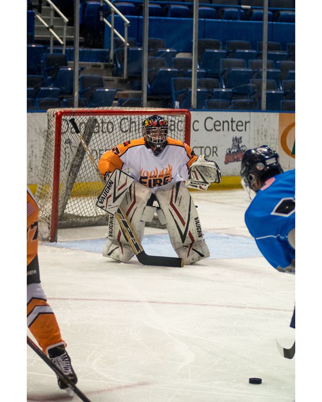 A hockey goalie in full gear defends the net during a game, stick in hand, ready for action.