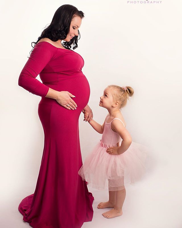 A mother expecting a baby poses with her young daughter in a studio setting, showcasing the bond and love between them.