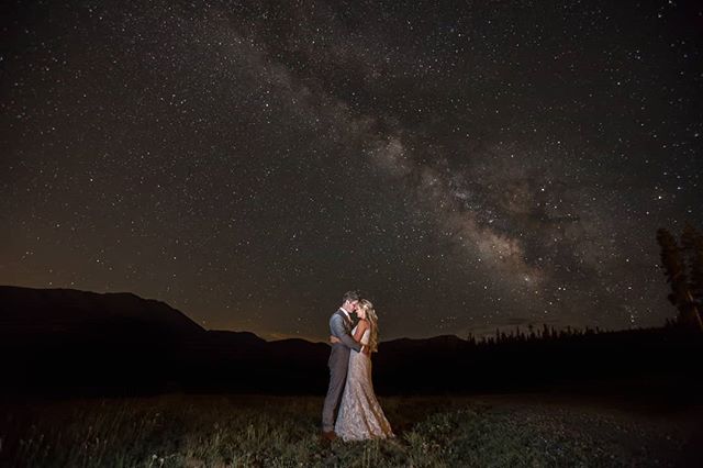 A bride and groom share a tender moment under a starry night sky in a romantic outdoor landscape.