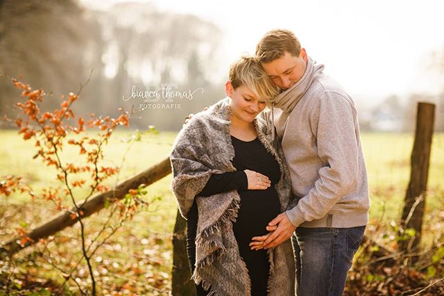 A loving couple embraces, the woman pregnant, in a sun-drenched field for a maternity photoshoot.