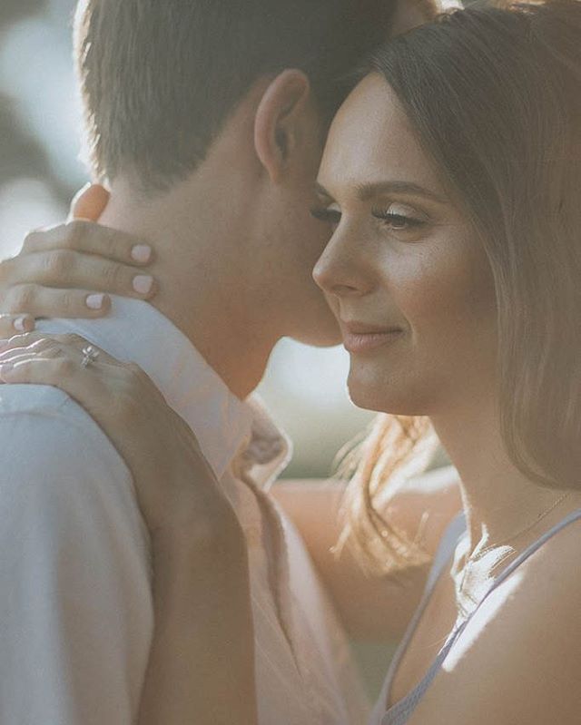 A couple shares an intimate moment, the woman's engagement ring subtly displayed.