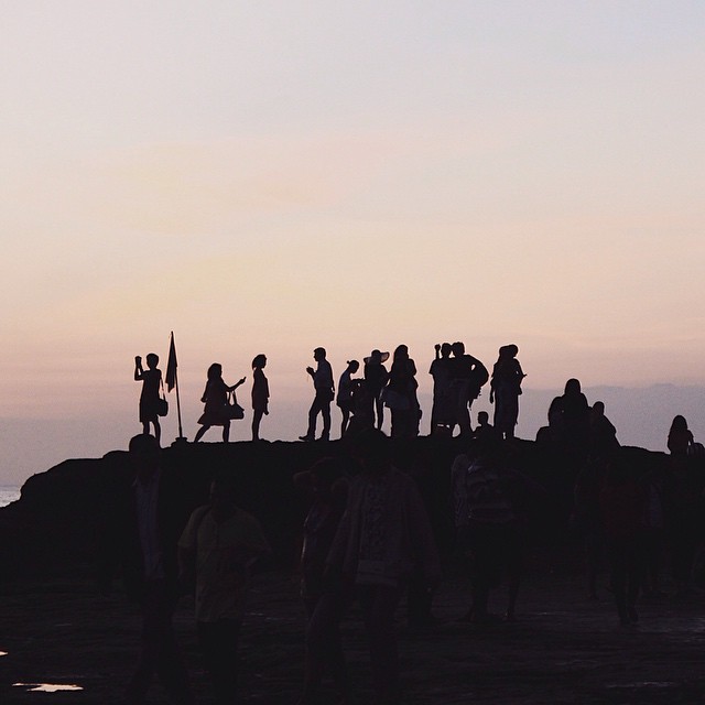 Silhouetted people gather on a beach at sunset, creating a tranquil and dreamy scene.