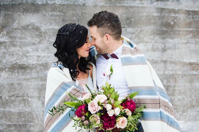 A newlywed couple embraces under a blanket during a romantic winter wedding with fresh snow.