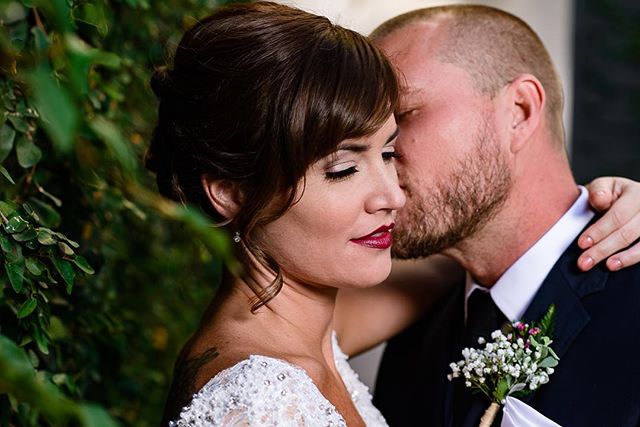 A bride and groom share an intimate moment, with the groom kissing the bride's cheek in soft, romantic light.