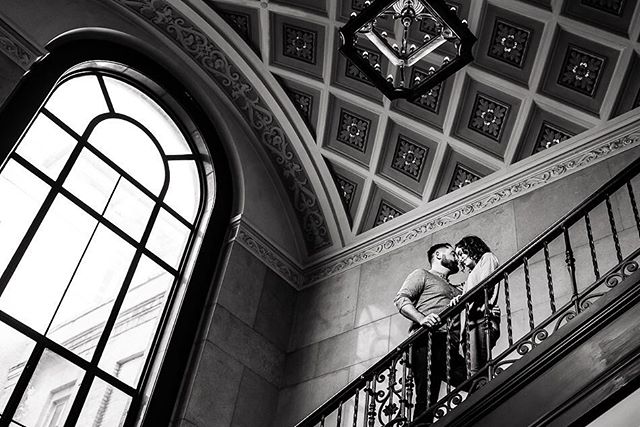 A couple in love shares a tender moment on a staircase in a grand building, captured in timeless black and white.