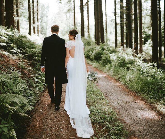 A newlywed couple walks hand-in-hand through a sunlit forest path, celebrating their special day in nature.