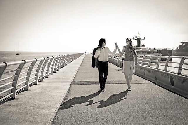 A couple holding hands as they walk along a pier. Black and white image perfect for travel or romance.