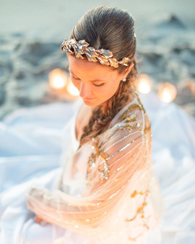 A bride with a gold leaf crown looks down, wearing a white and gold wedding dress.