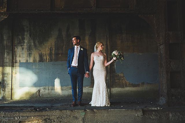 A bride and groom hold hands in front of an industrial wall, posing for their wedding photos.
