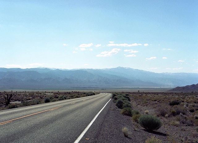 A long road stretches through the desert towards mountains under a clear sky. Scenic landscape ideal for travel and adventure themes.